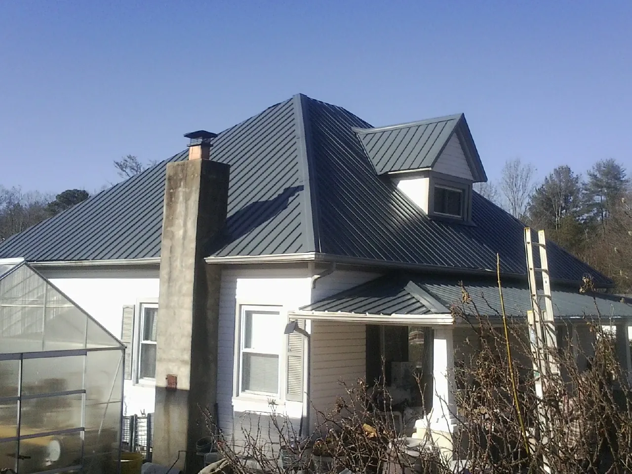 Dark blue standing seam metal roof on a white farmhouse with dormer — Slate & Tile Roof Repair by Roofing Brothers in La Pine