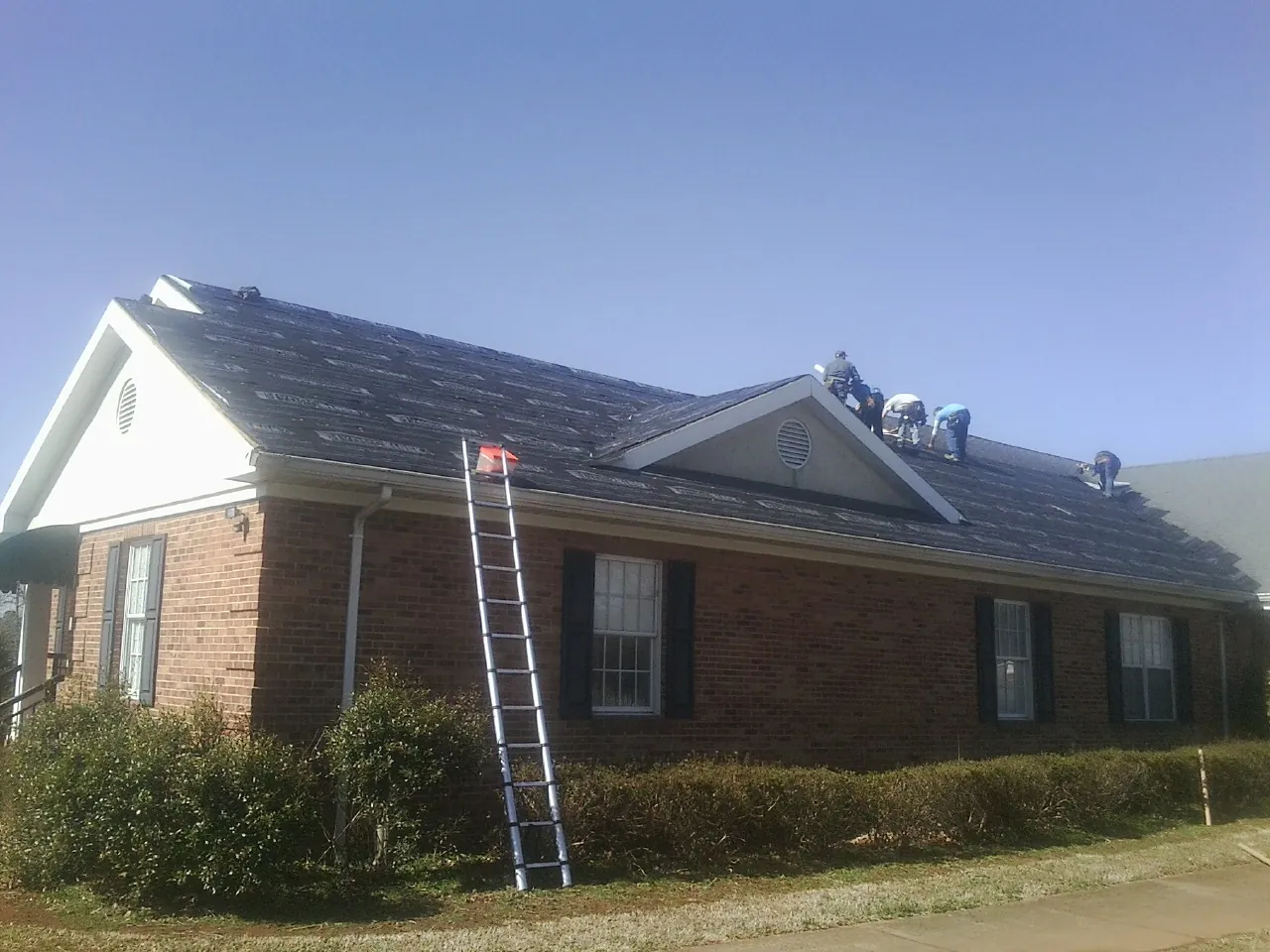 Crew tearing shingles off a brick ranch roof with a ladder set — Metal Roof Repair work by our crew in La Pine