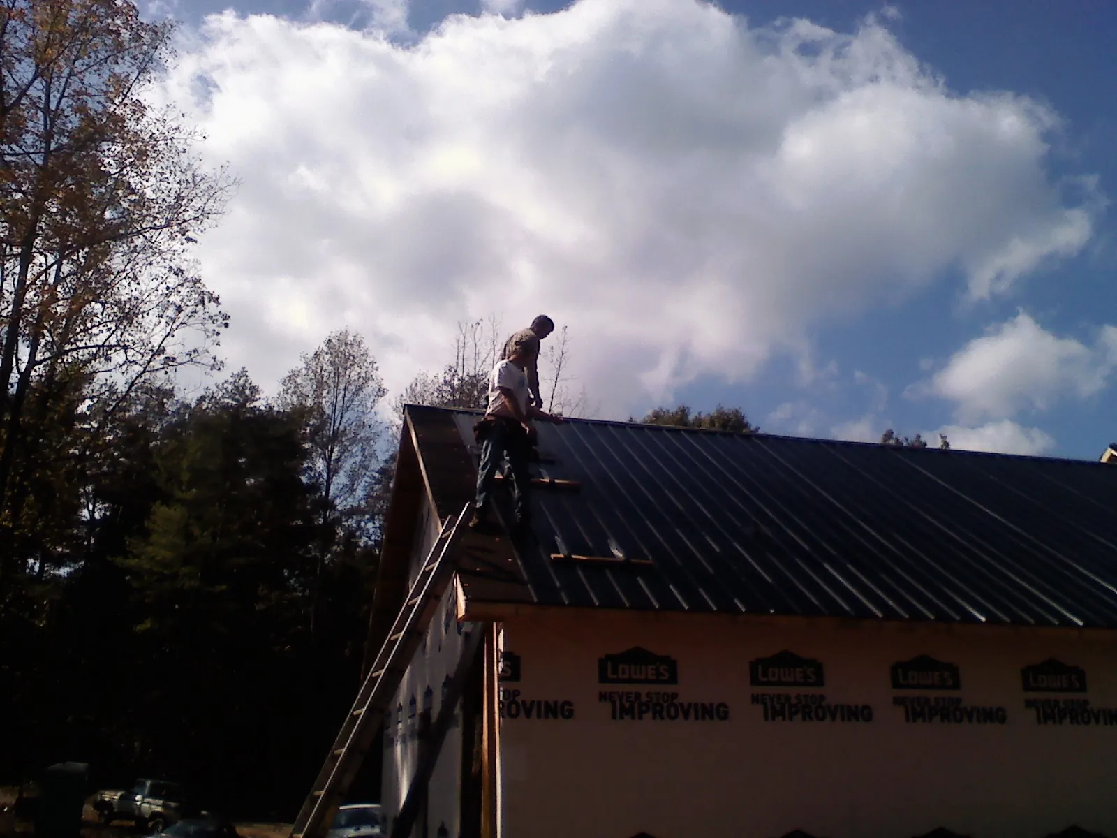 Roofer fastening dark metal panels high against a cloudy sky, from a Roof Inspection job in La Pine