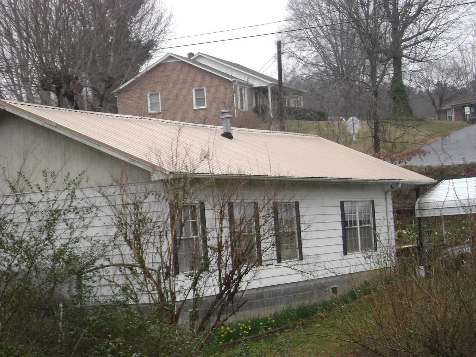 Tan metal roof on a white sided house set into a hillside — Commercial Roofing by Roofing Brothers in La Pine